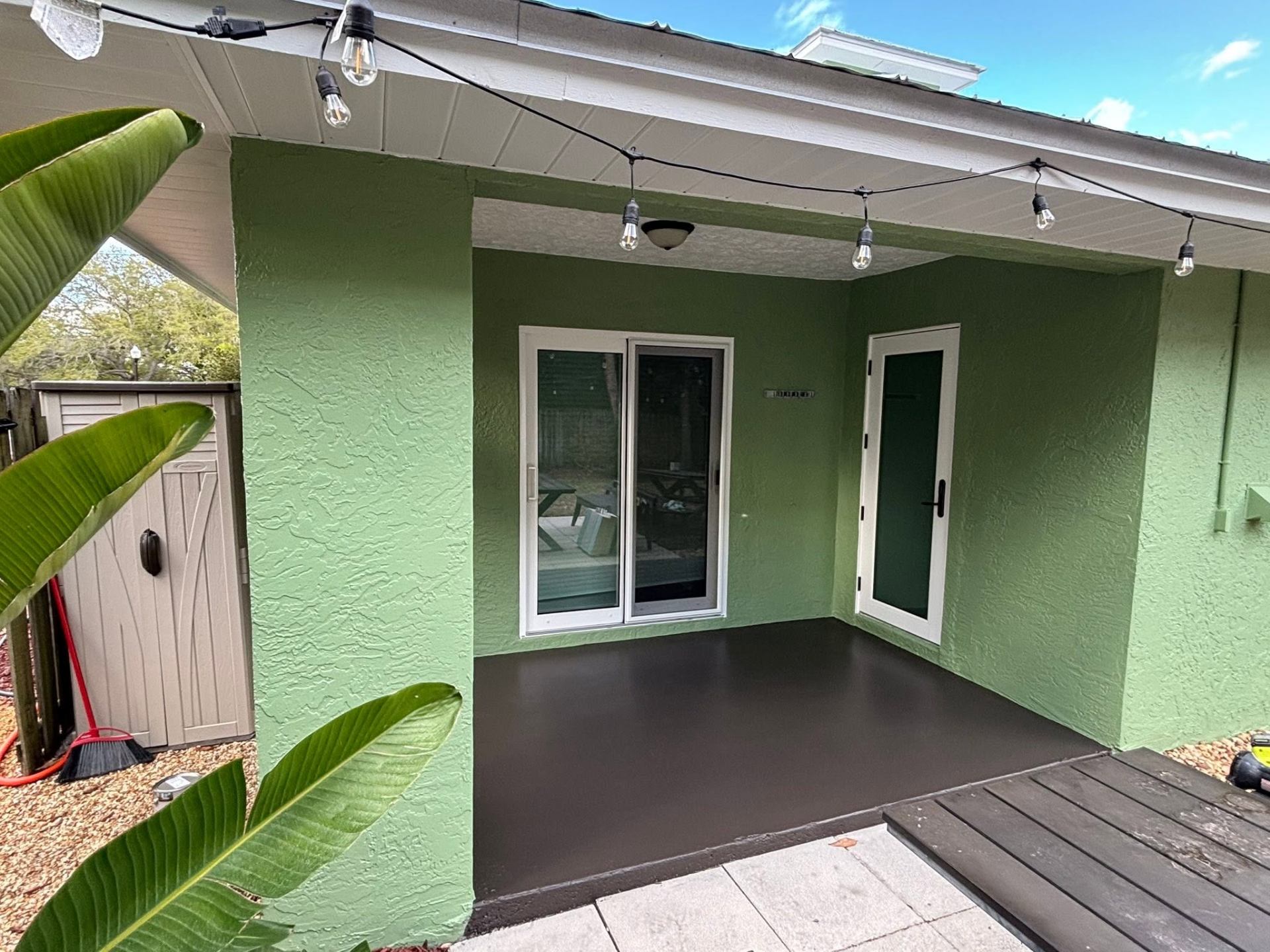 Freshly sealed dark charcoal patio floor against green stucco walls at a Treasure Coast home by Millman Services.